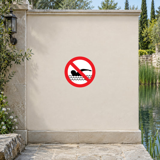 NO Safety Sign Sticker applied in ornamental park pond edge, smooth solid cream masonry wall, pond water and reeds at extreme sides