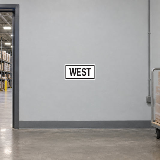 Road Sign Sticker applied in A light grey warehouse wayfinding corridor wall with pallet cart at extreme right and doorway far left, blank smooth center