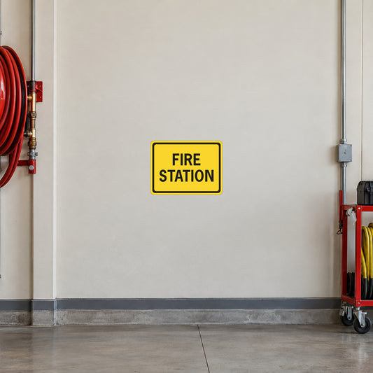 Road Sign Sticker applied in A cream fire station vehicle bay wall with red hose coil far left and equipment trolley low right, blank smooth center