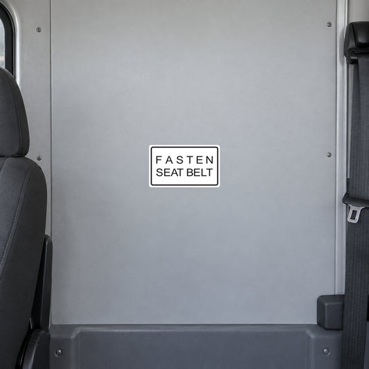 Road Sign Sticker applied in A light grey shuttle bus interior flat smooth partition panel behind driver, seatbelt extreme right and seat edge far left, uninterrupted blank center