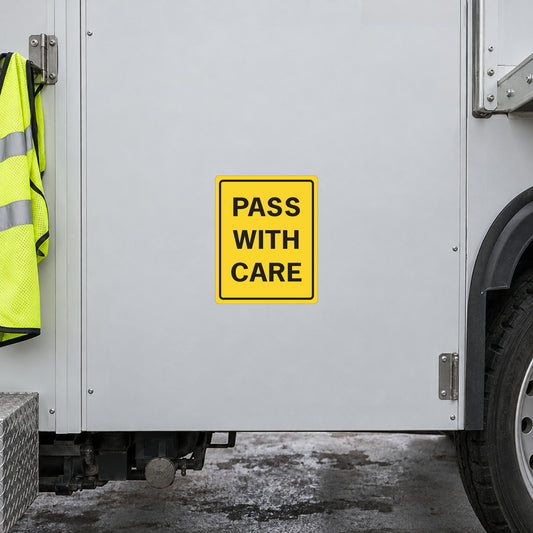 Yellow road sign sticker with black text: PASS WITH CARE.