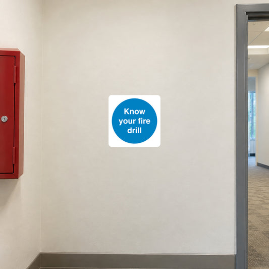 Safety Sign Sticker applied in a smooth pale cream wall in a workplace fire drill briefing alcove, closed fire action document box extreme left and corridor doorway far right
