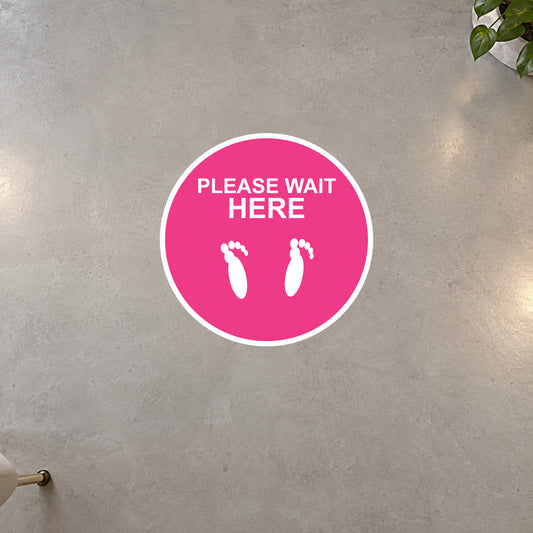 Pink circular “PLEASE WAIT HERE” non-slip floor sticker with white foot icons