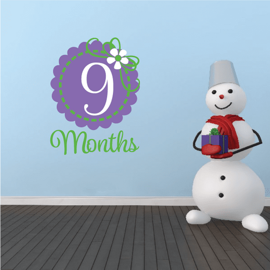 Purple 9 months wall decal with flower accents and green lettering, plus smiling snowman