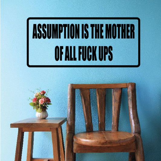 Rectangular wall decal with black text: 'ASSUMPTION IS THE MOTHER OF ALL FUCK UPS'