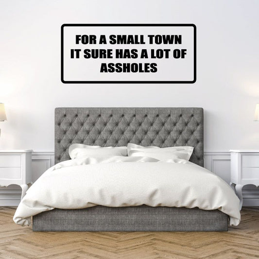 Rectangular wall decal with bold black text: FOR A SMALL TOWN IT SURE HAS A LOT OF ASSHOLES