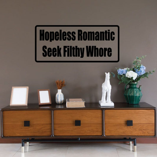 Rectangular black-bordered wall decal with bold text 'Hopeless Romantic' and 'Seek Filthy Whore'.