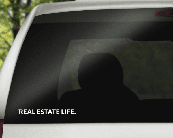 Horizontal window decal with "REAL ESTATE LIFE." text on dark car glass