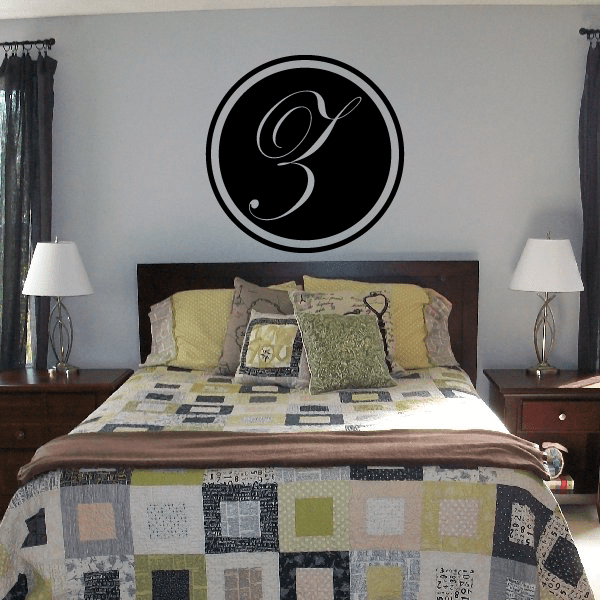 Black circular monogram decal with gold cursive letter above bed