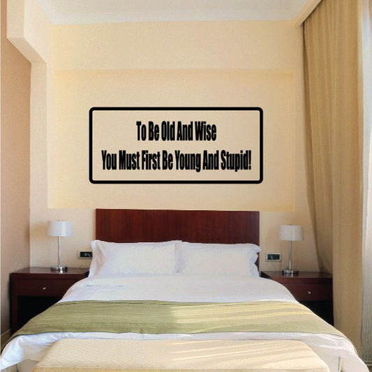 Rectangular wall decal, black border, reads: To be old and wise; be young and stupid