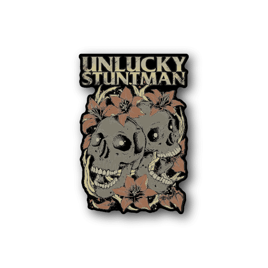 Vinyl sticker with Unlucky Stuntman text, twin skulls and leaves, tan.