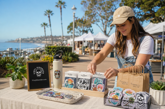 Custom Vinyl Disorder sticker packs displayed at a sunny Dana Point outdoor market
