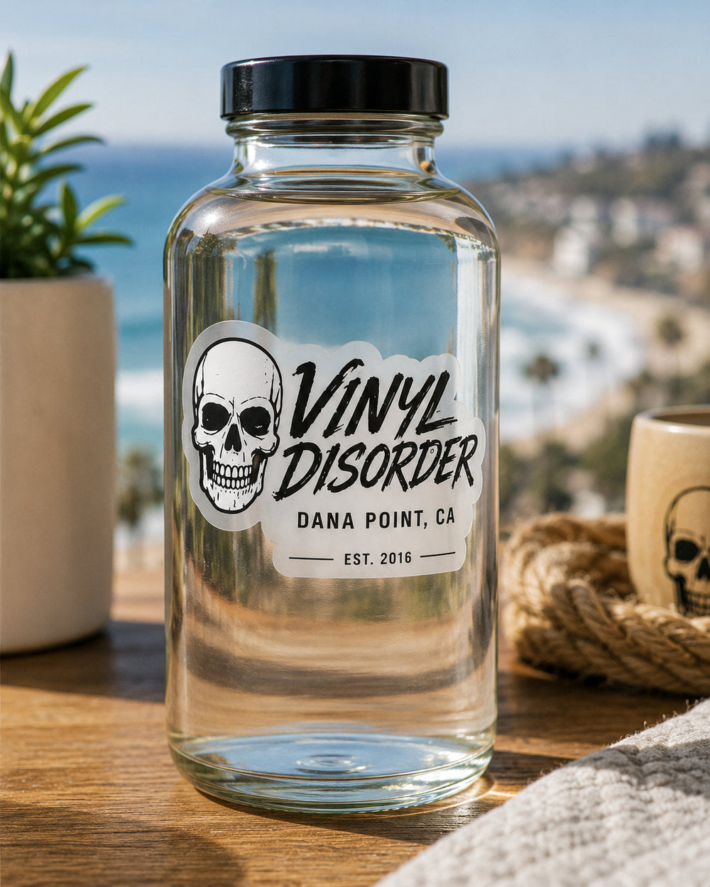 Clear Vinyl Disorder sticker with white backing applied to a glass bottle in a coastal setting