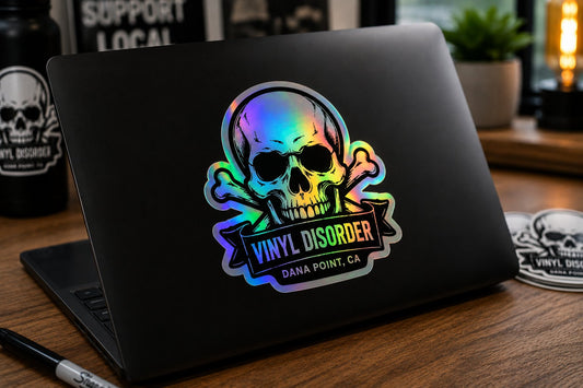 Holographic Vinyl Disorder sticker on a black laptop in a moody creative workspace