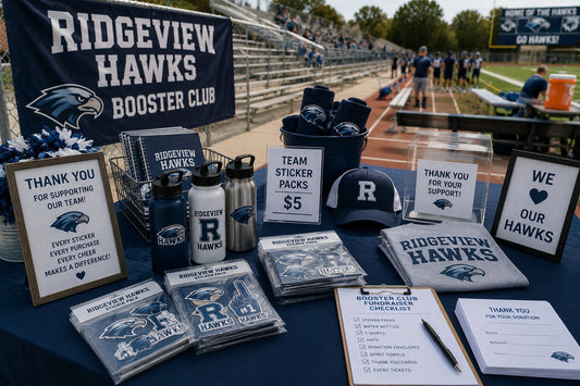 Fictional Ridgeview Hawks booster club fundraising table beside the field with sticker packs, bottles, spirit gear, donation materials, and supporter signage