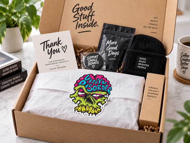 Open subscription box with colorful Vinyl Disorder sticker, tissue paper, thank-you card, and neatly packed products