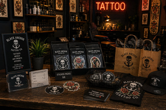 Fictional tattoo shop retail counter with sticker packs, appointment cards, shirts, hats, bags, art prints, and studio merchandise