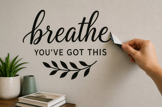 Adult hand gently lifting the corner of a simple black wall decal from a light painted wall in a clean home interior