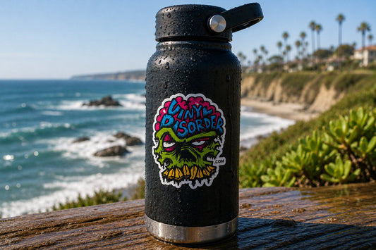 Vinyl Disorder sticker on a black insulated bottle covered with water droplets at a sunny coastal overlook
