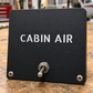 Black aircraft label plate with CABIN AIR text and two front mounting screws