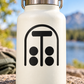 Vinyl decal crest with black arched border, T shape, and four dots on white bottle