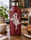 White vinyl decal of rockabilly devil girl baking with flames on maroon bottle