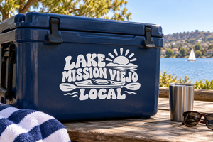 White vinyl decal on dark blue cooler: sun, waves, 'LAKE MISSION VIEJO LOCAL'.