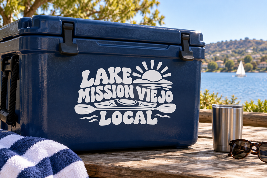 White vinyl decal on dark blue cooler: sun, waves, 'LAKE MISSION VIEJO LOCAL'.