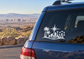 Black vinyl decal of desert skyline with palm trees, starburst, and atomic-style wheel on car glass