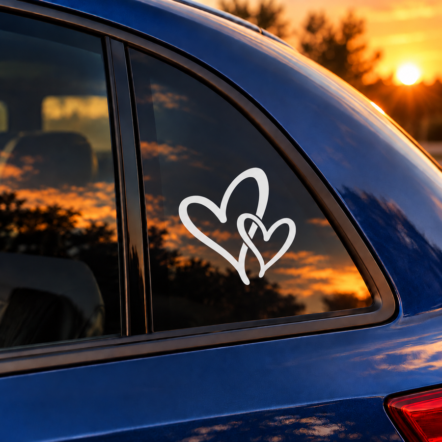 White interwoven heart vinyl decal with flowing tails on a car window.
