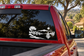 Black vinyl sailboat horizon decal on car rear window with trees, lake, and small sailboat