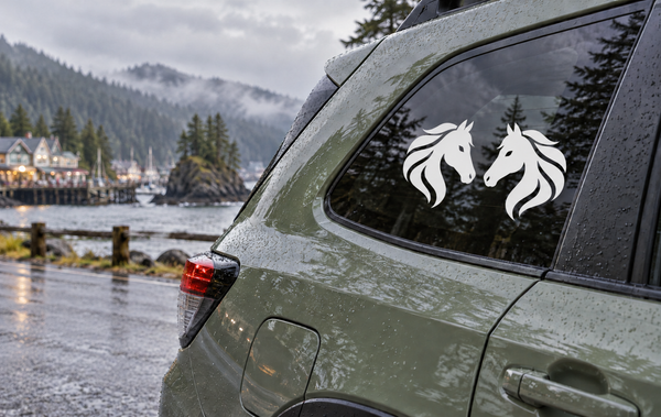 Vinyl decal with two black horse heads and white flowing manes on a car window
