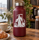 Vinyl decal graphic of a cloaked reaper with scythe and garden plants on a dark red bottle