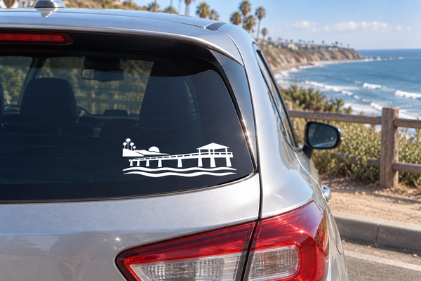 Vinyl car decal of a pier with waves and palm trees on rear window, white design.