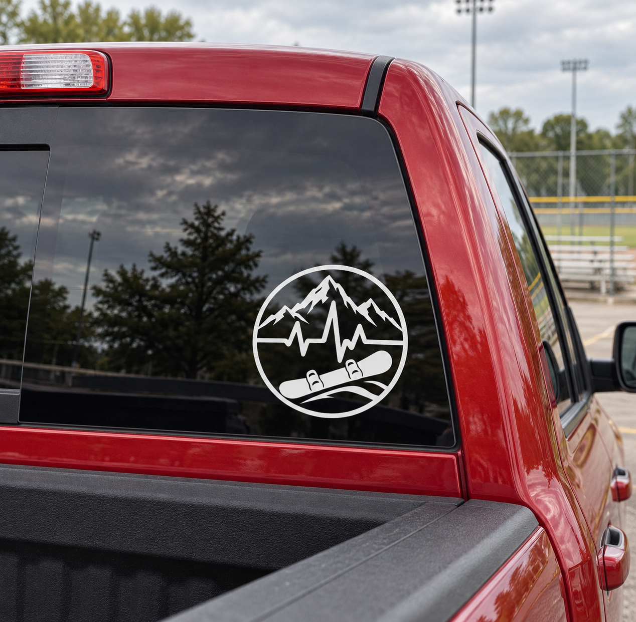Round vinyl decal with mountain peaks, heartbeat line, and snowboarder boots on red car glass