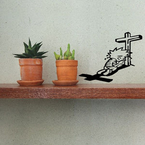 Black wall decal of a praying figure beside a cross