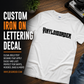 Iron-on lettering decal with black stylized text on a white short-sleeve shirt