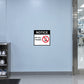 No Smart Phone Notice Sticker applied in a pale blue flat wall beside a precision electronics laboratory entrance, cleanroom shoe station visible at bottom left edge, central broad smooth surface