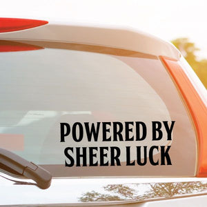 Powered By Sheer Luck decal in bold black letters on a clear surface