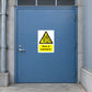 Caution Risk Of Explosion Sticker applied in Closed heavy muted blue gas-storage access door in a secure industrial courtyard, broad flat central surface, lock far left, ventilation grille only above top door edge and concrete ground below.