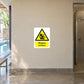 Caution Slippery Surface Sticker applied in Smooth pale tan wall beside a swimming facility wet changing-area walkway, central clear panel frontal, tiled floor below and shower entrance only at far right.