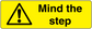 Bright yellow warning sticker with black triangle exclamation and text 'Mind the step'