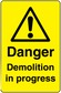 Yellow warning sticker with black triangle exclamation and text “Danger Demolition in progress”