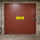 Danger Asbestos Yellow Sticker applied in Closed broad muted red restricted maintenance door in an older civic building basement, central smooth surface clear, latch far right, stone jamb and protected flooring at margins.