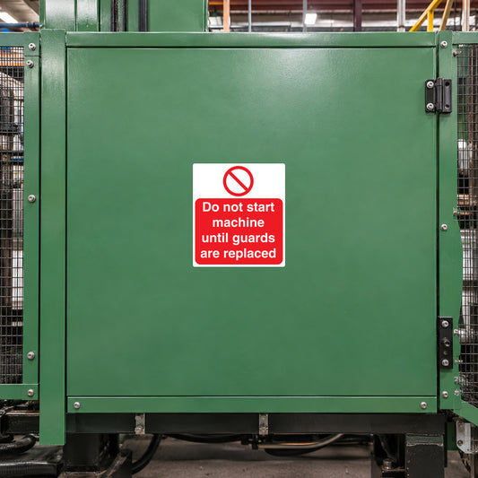 Safety sticker on green industrial machine panel: 'Do not start machine until guards are replaced'