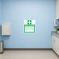 Emergency First Aiders Sticker applied in Blank smooth pale blue wall in a commercial printing first aid corner, small unmarked medical cabinet below y80%, sink at far right, linoleum flooring.