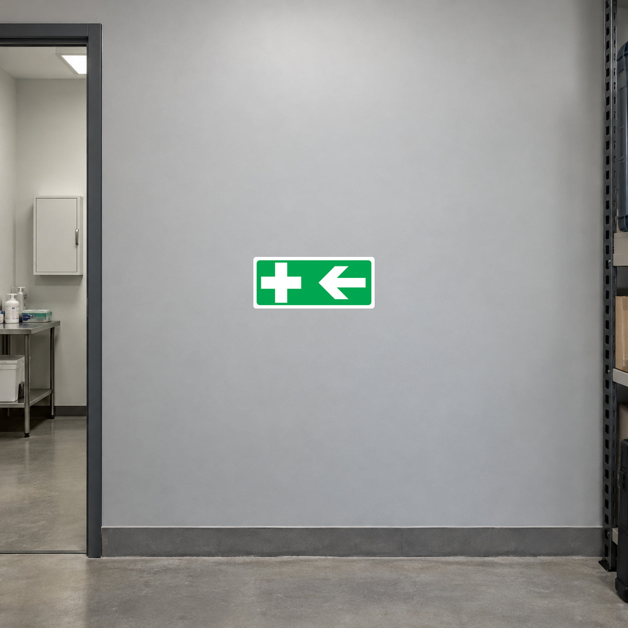 Aid Left Sticker applied in Blank smooth soft gray wall in an electrical workshop staff corridor, first aid room doorway at extreme LEFT, unmarked medical cabinet visible inside, clean concrete floor.