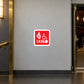Handicap Fire Exit Sticker applied in a theatre accessible escape corridor, smooth pale gray wall, a wide level wheelchair-accessible exit doorway at far RIGHT, no steps, flat dark vinyl floor, brass door trim left