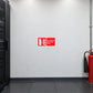 Use On Electrical Fires Sticker applied in a commercial broadcast control equipment room, smooth cool white wall, red CO2 extinguisher with black horn far lower right, closed black equipment rack edge left, raised dark antistatic floor