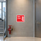 Wet Riser Sticker applied in a modern high-rise office fire-service landing, smooth warm gray concrete wall, red wet-riser outlet valve below y=82%, glazed stairwell edge left and silver door edge right, pale terrazzo floor
